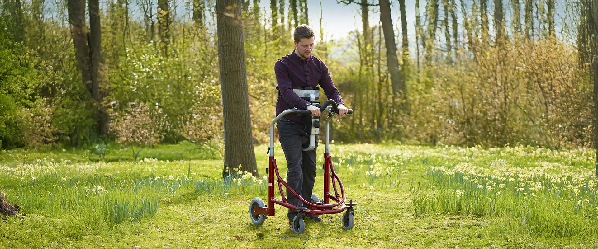 Man using a Meywalk walker in a park with trees and flowers.