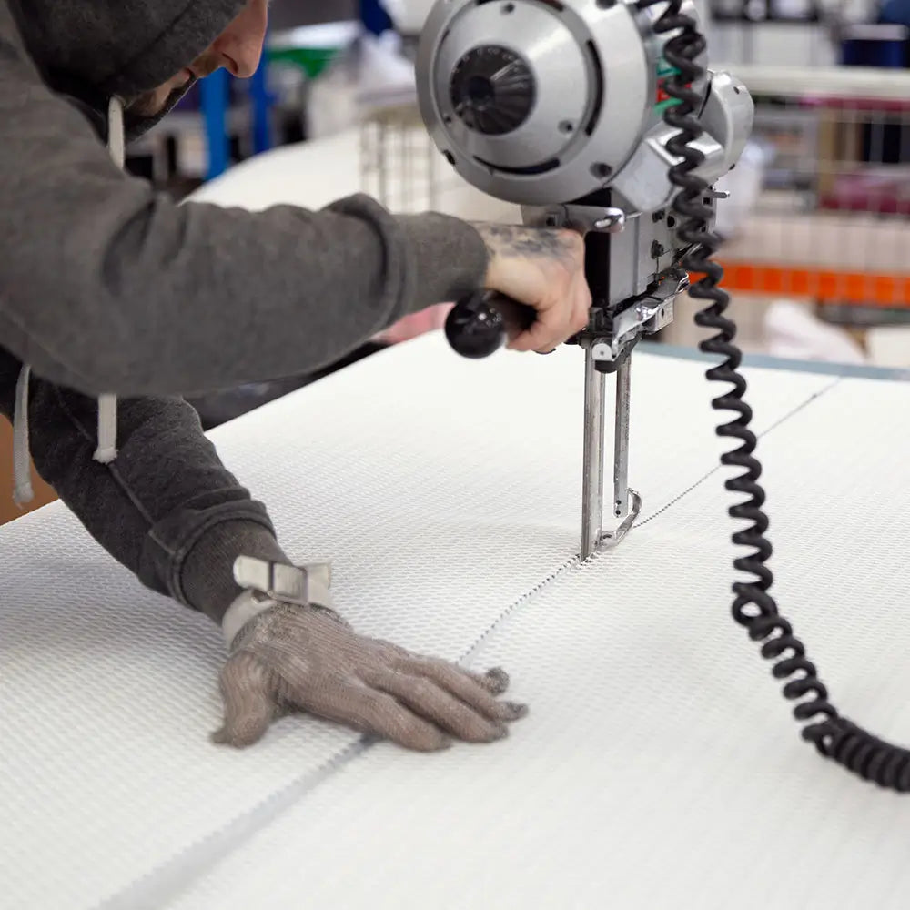 Person using a cutting tool on white material in a factory setting.