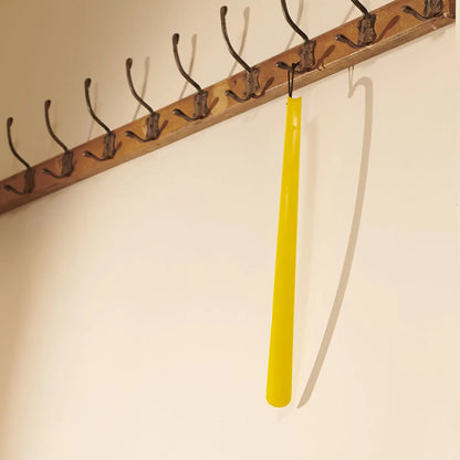 Yellow shoe horn hanging from a wooden peg rack on a beige wall.