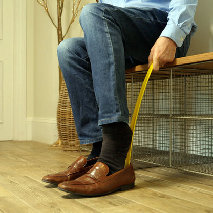 A person sitting on a bench using a yellow shoe horn to put on their shoes