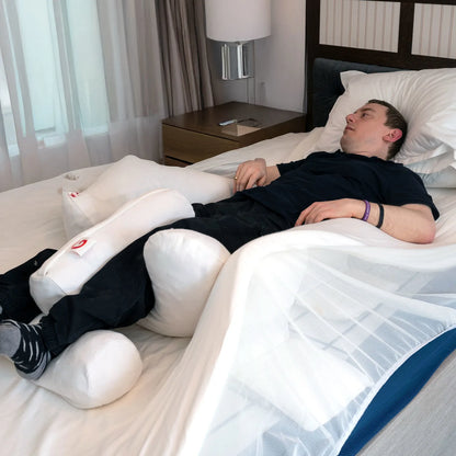 Person lying on a bed with supportive pillows in a bedroom setting