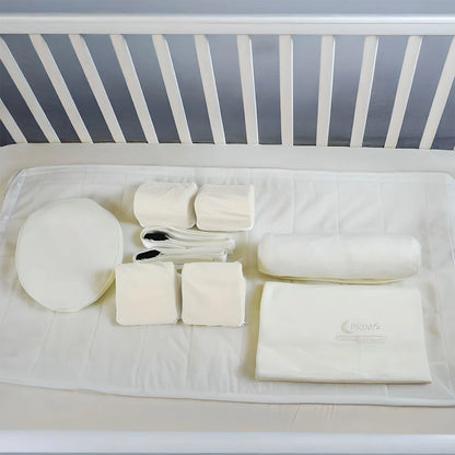 Baby crib with white bedding and accessories on a plain background